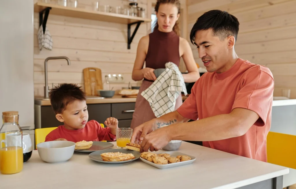 Criança comendo na mesa com os pais, aprendendo autonomia alimentar infantil
