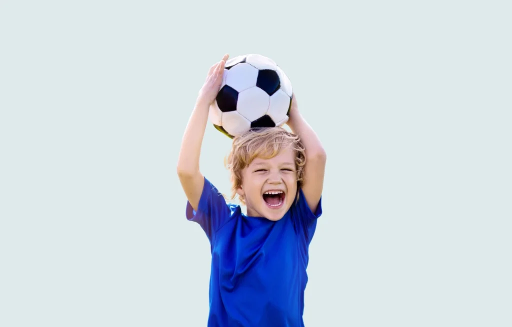 Criança feliz segurando uma bola de futebol acima da cabeça, simbolizando apoio dos pais sem cobrança