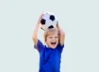 Criança feliz segurando uma bola de futebol acima da cabeça, simbolizando apoio dos pais sem cobrança