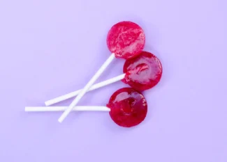 Três pirulitos vermelhos em fundo roxo para quiz sobre engasgo infantil
