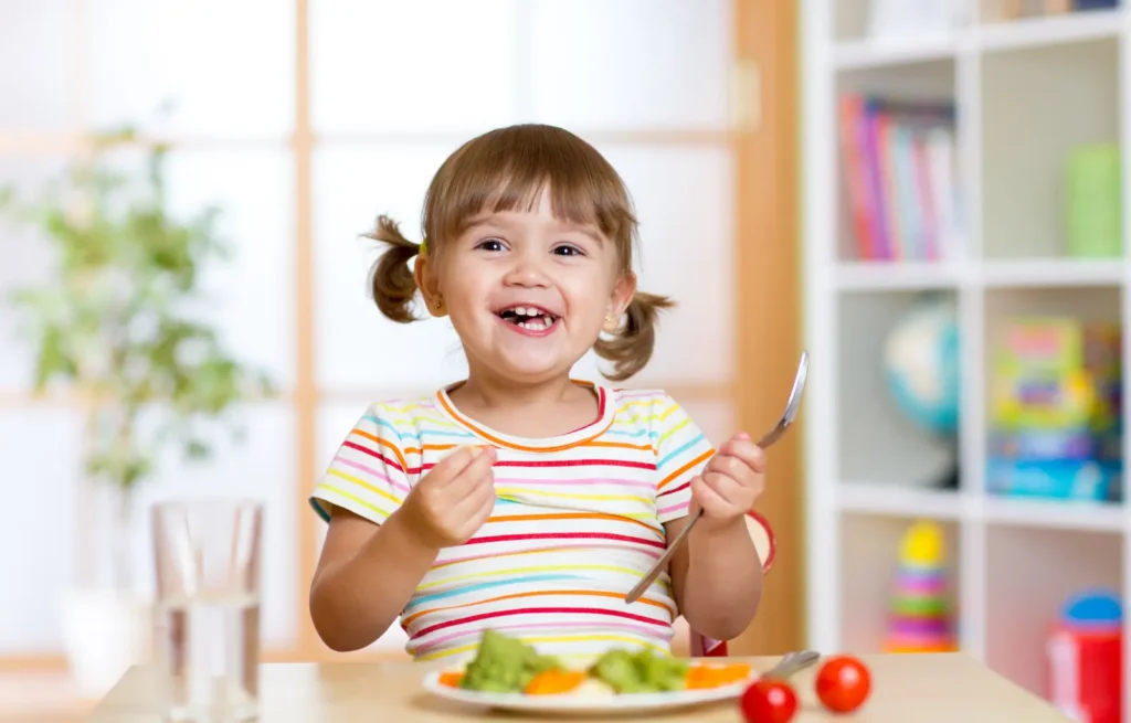 Criança sorridente comendo legumes coloridos, exemplo de alimentação infantil saudável
