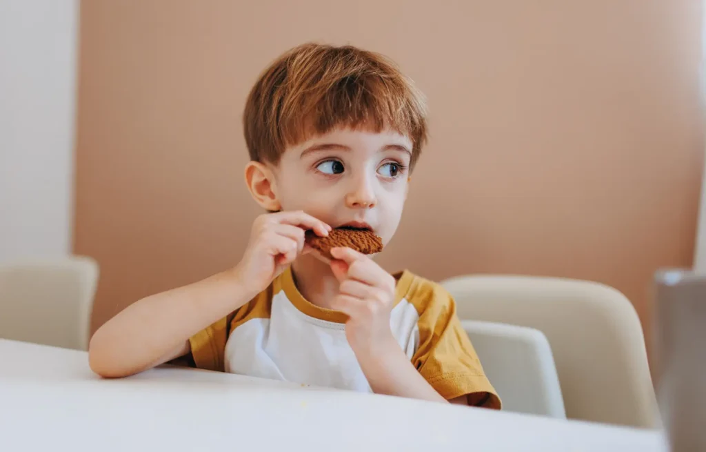 Criança comendo cookie de chocolate sem açúcar, um dos doces do cardápio de Dia das Crianças saudável