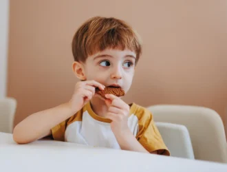 Criança comendo cookie de chocolate sem açúcar, um dos doces do cardápio de Dia das Crianças saudável