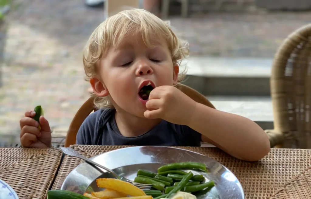 Paladar infantil: criança comendo vagem com as mãos, com pepino e batata frita no prato
