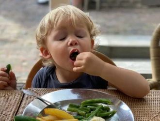 Paladar infantil: criança comendo vagem com as mãos, com pepino e batata frita no prato