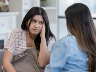 Como lidar com filhos adolescentes: Filha adolescente com expressão de desânimo ouvindo a mãe durante uma conversa no sofá de casa
