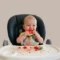 Bebê na cadeira de alimentação comendo uma fatia de melancia com as mãos durante a introdução alimentar do bebê